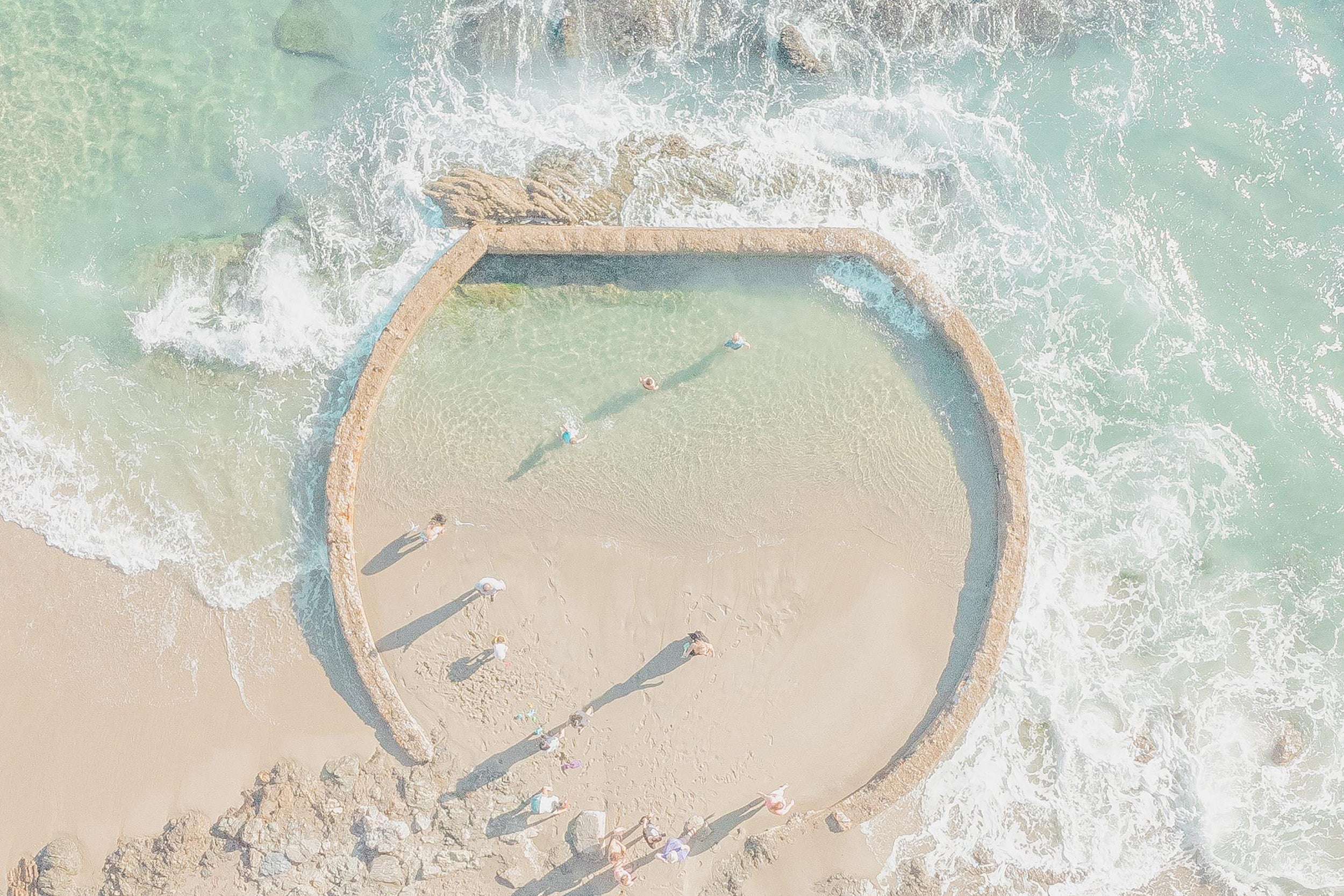 A circular sandbar with people walking on it, surrounded by ocean water.