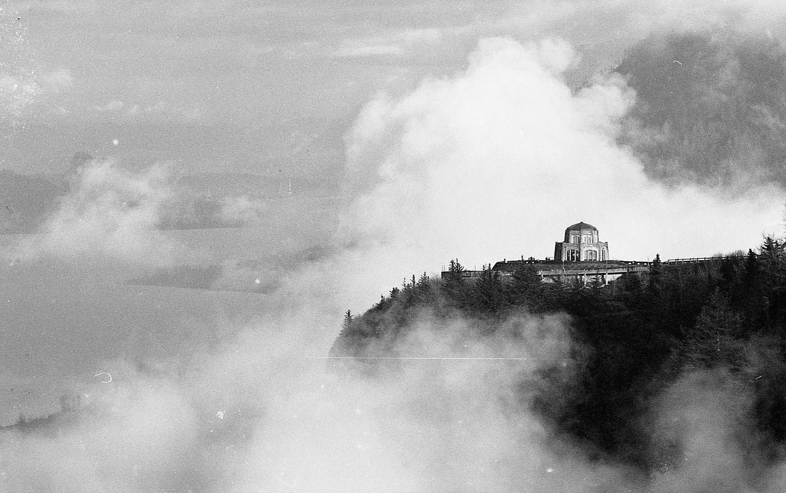 Historical black and white photograph of a building on a hill shrouded in clouds