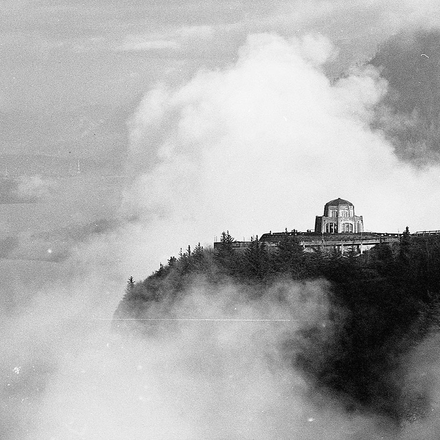 Historical black and white photograph of a building on a mountain peak with clouds surrounding it.