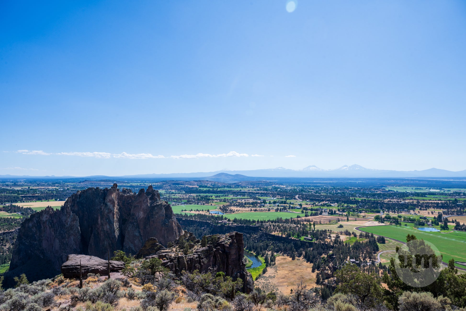 Scenic view of a rocky landscape with fields and mountains under a clear blue sky.