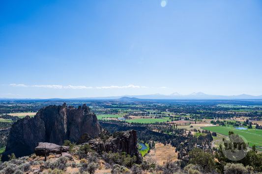 Scenic view of a rocky landscape with fields and mountains under a clear blue sky.